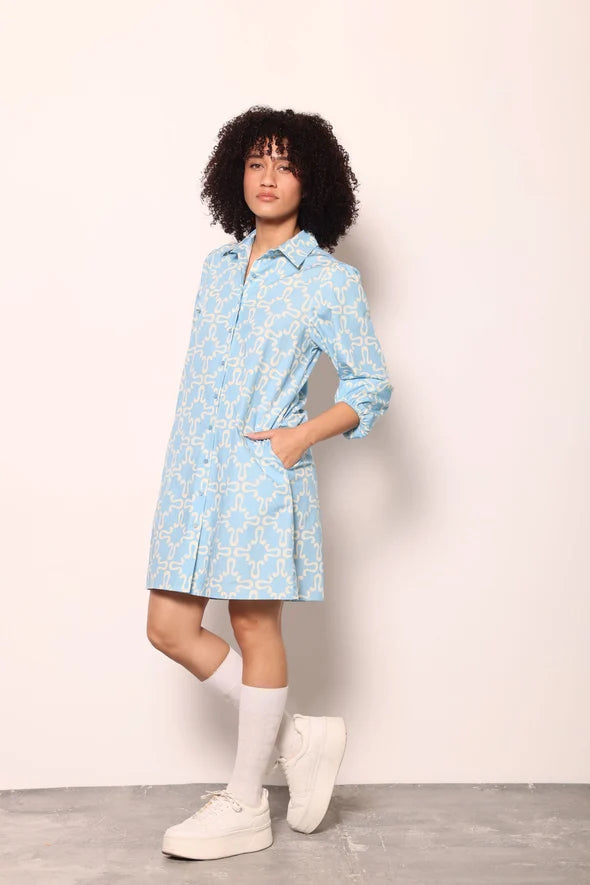
Woman wearing the Maude Vivante Ava Dress in Carolina Blue, featuring a vibrant blue print, collared button-front design, three-quarter balloon sleeves, contrast trim, and a relaxed A-line silhouette.