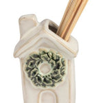 Four small ceramic toothpick holders shaped like a house with a green wreath, a snowman, a Santa figure, and a Christmas tree, arranged in a row on a white background.