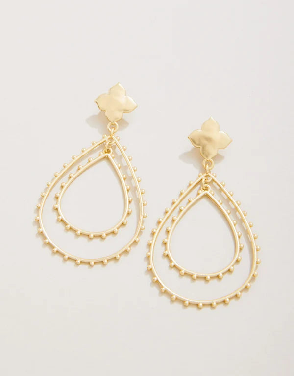 A pair of gold-tone dangle earrings with a small flower-shaped stud and two layered teardrop-shaped wire frames outlined with tiny bead details, shown on a light off-white background.