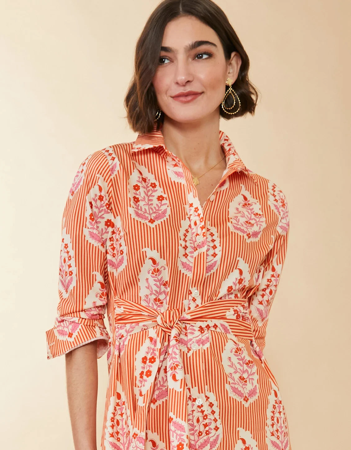 Woman wearing an orange and pink patterned dress against a beige background