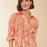 Woman wearing an orange and pink patterned dress against a beige background