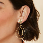 Gold earrings worn by a person with a neutral background
