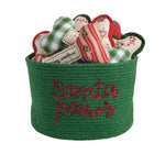 Green basket with 'Santa Paws' text containing Christmas-themed dog toys on a white background