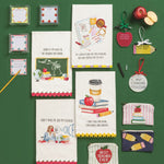 A flat-lay display of various school-themed paper goods and small accessories on a dark green background. The collection includes greeting cards, small note cards, a coffee mug tag, a 'Best Teacher Ever' ornament, a 'Don't Make Me Que My Teacher' card, a 'Don't Make Me Que My Teacher' pouch, and other matching school-themed items.
