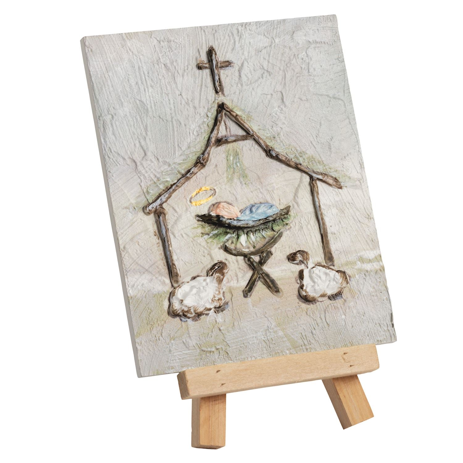 A small canvas painting of a nativity scene displayed on a wooden easel against a plain white background. The artwork shows a stable with a cross, a baby in a manger with a blue blanket and yellow halo, and two sheep.