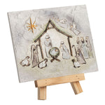 A small rectangular canvas or panel featuring a hand-painted nativity scene, displayed on a simple wooden easel against a plain white background.