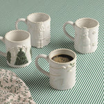 Four white ceramic mugs with embossed holiday illustrations, arranged on a green and white striped fabric background. One mug in the foreground contains coffee, and a matching patterned cloth is partially visible in the lower left corner.