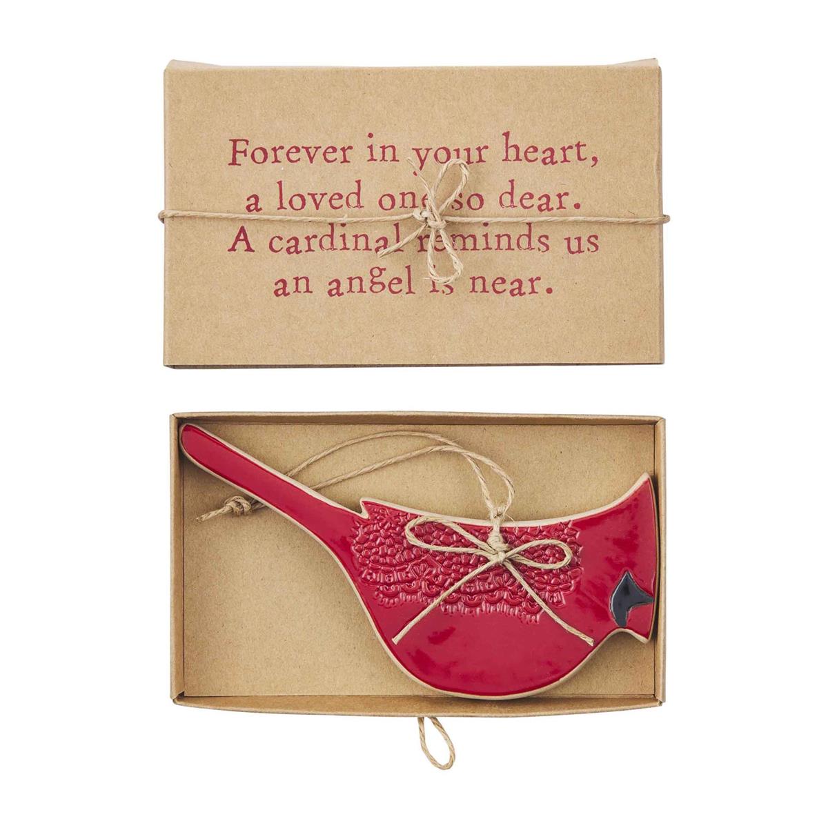A red bird-shaped ornament with white floral embroidery and a small black cardinal head, displayed in an open kraft gift box with a hanging string. The box lid above reads, 'Forever in your heart, a loved one so dear.
