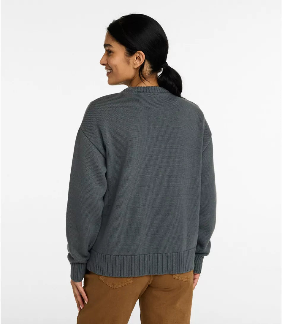 A woman shown from the back wearing a dark gray knit sweater and brown pants against a plain white studio background.