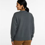 A woman shown from the back wearing a dark gray knit sweater and brown pants against a plain white studio background.