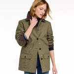 A woman wearing an olive green utility jacket with dark brown corduroy collar and cuffs, featuring small embroidered details, paired with blue jeans against a white studio background.
