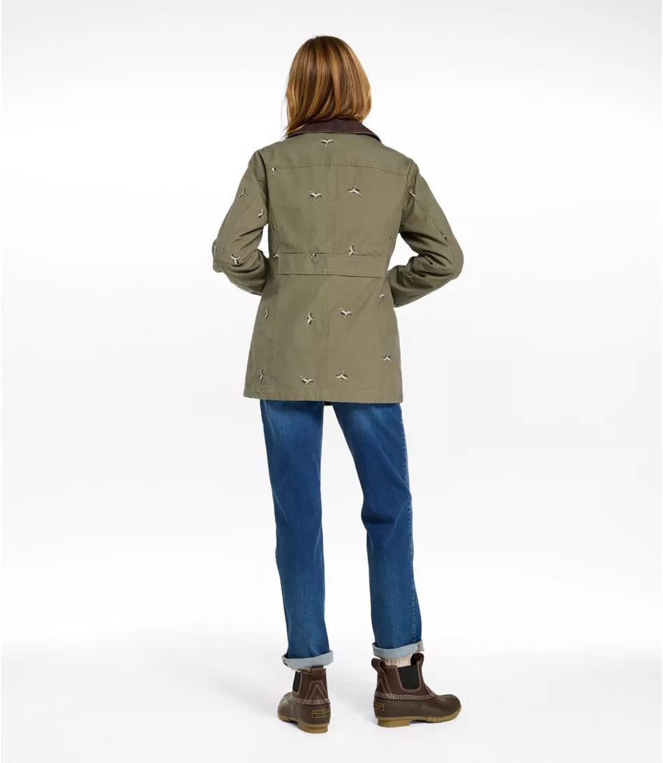 A woman shown from the back wearing an olive green jacket with small bird motifs, blue jeans, and brown boots against a plain white studio background.