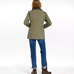 A woman shown from the back wearing an olive green jacket with small bird motifs, blue jeans, and brown boots against a plain white studio background.