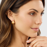 Close-up of a woman wearing gold earrings with a neutral background