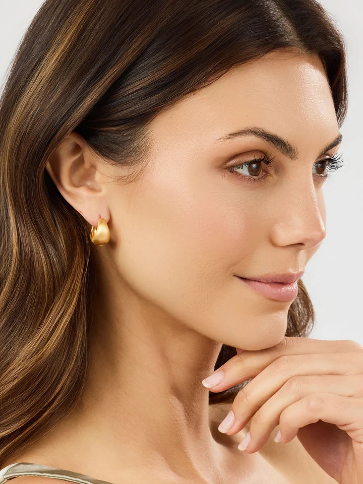 Close-up of a woman wearing gold earrings with a neutral background