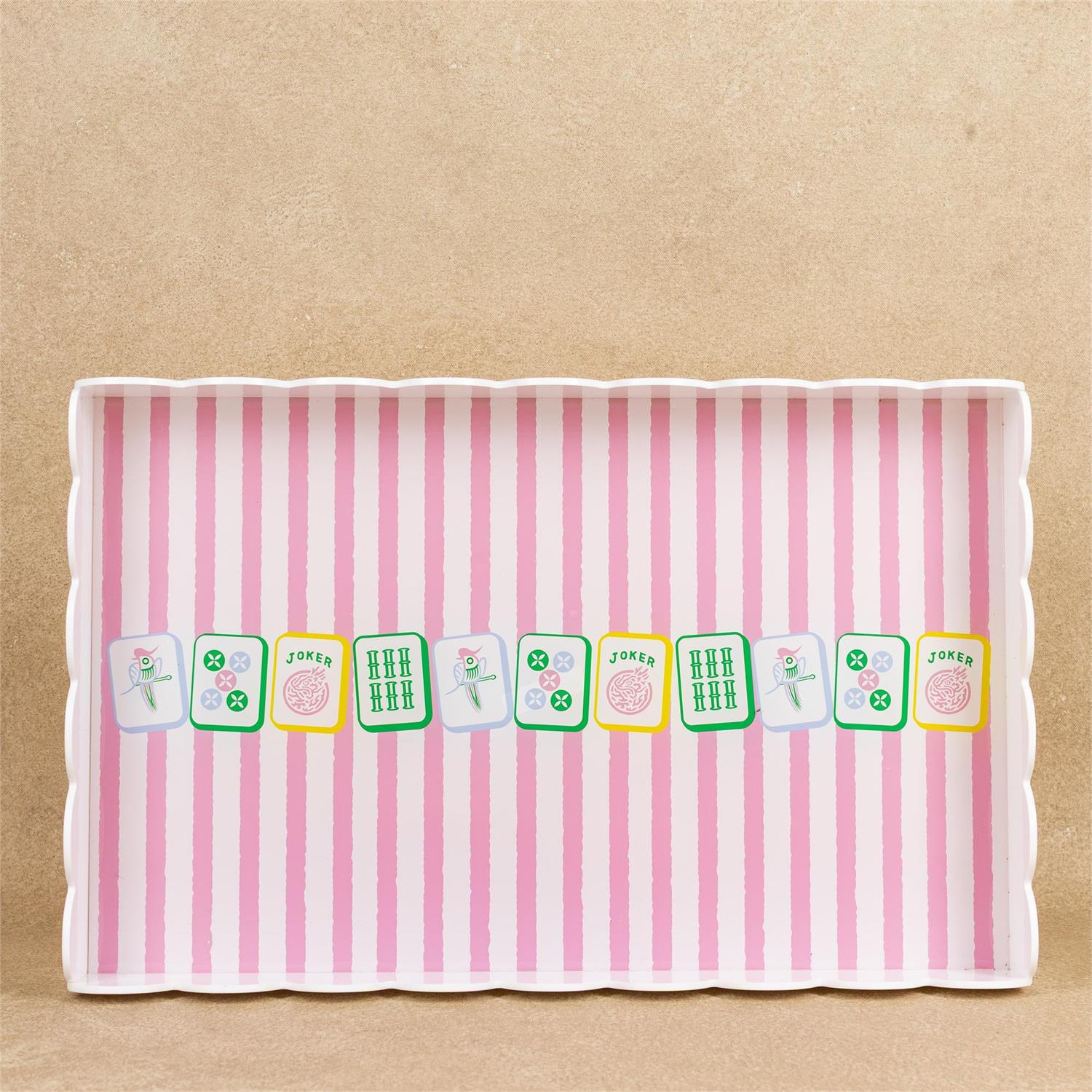 A rectangular serving tray with scalloped edges, featuring a pink and white vertical stripe pattern and a row of illustrated mahjong tiles across the center, set against a textured beige background.