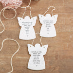 Three white angel-shaped ornaments with inscriptions on a wooden surface