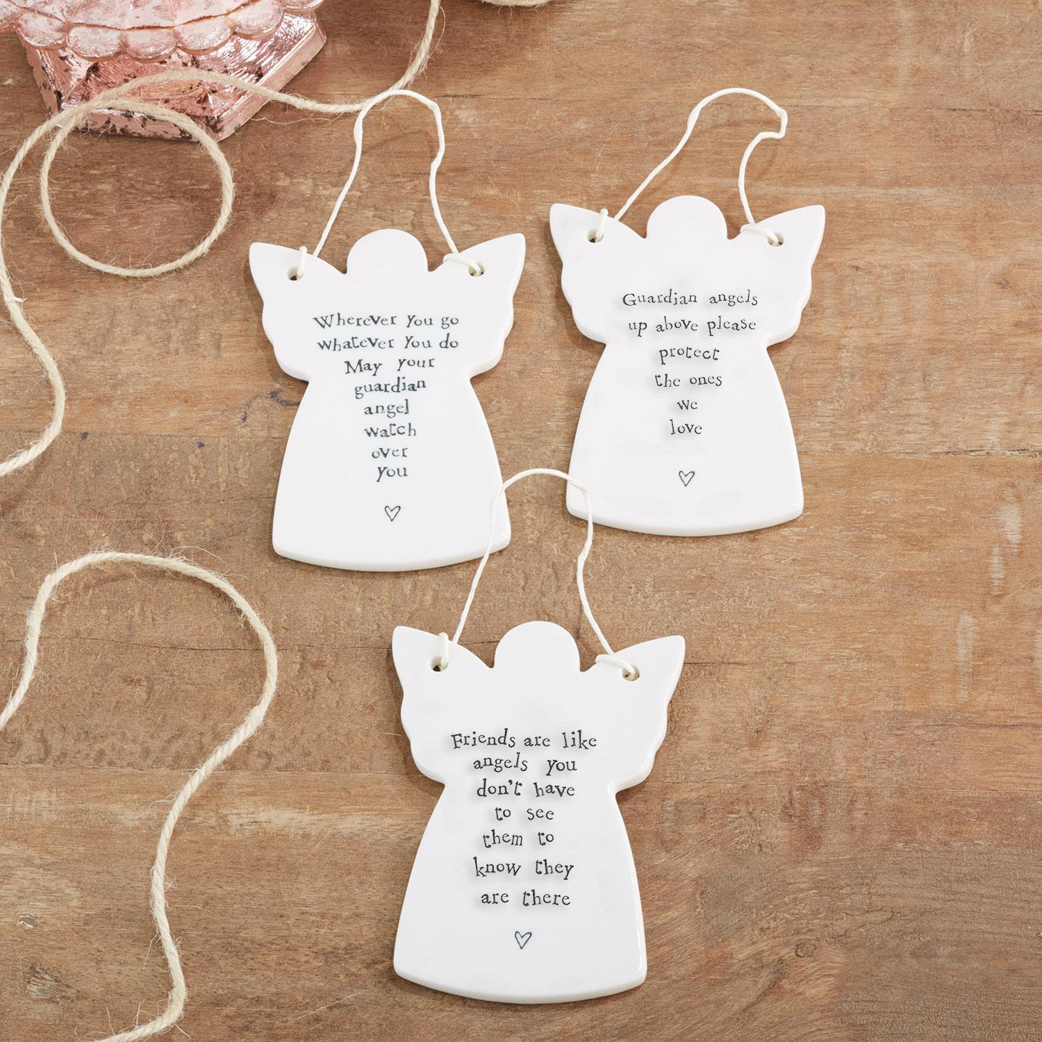 Three white angel-shaped ornaments with inscriptions on a wooden surface