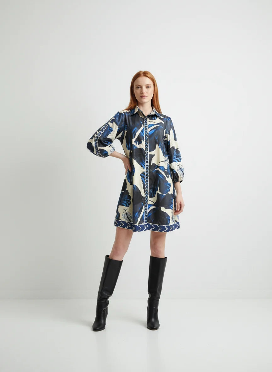 Woman wearing the Maude Vivante Ava Dress in Indigo Lilies, featuring a blue floral print, collared button-front design, three-quarter balloon sleeves, and black knee-high boots.