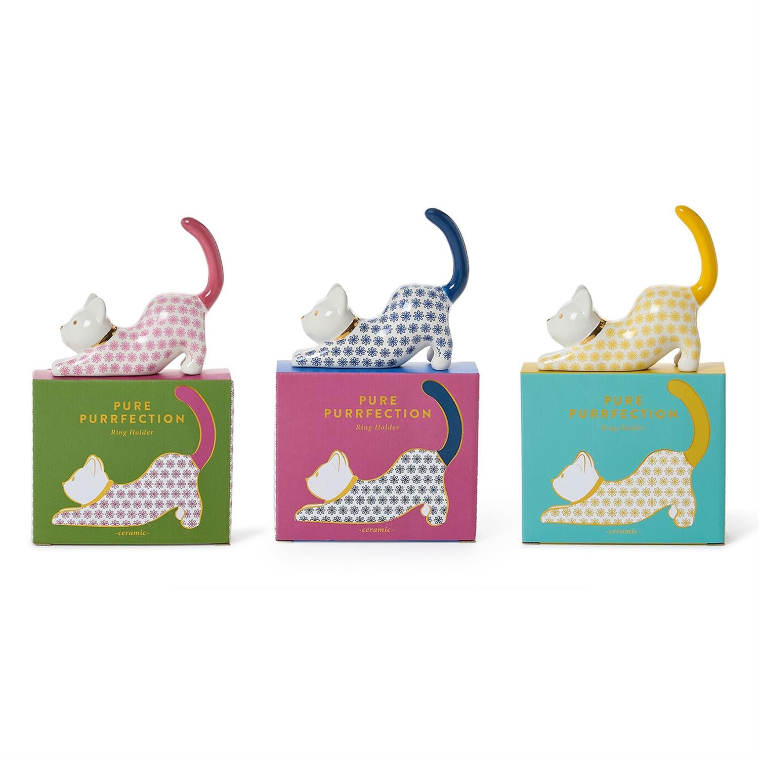 Three small ceramic cat figurines in different colors, each standing on its own illustrated box. The left cat is pink and white with a pink tail, on a green box.