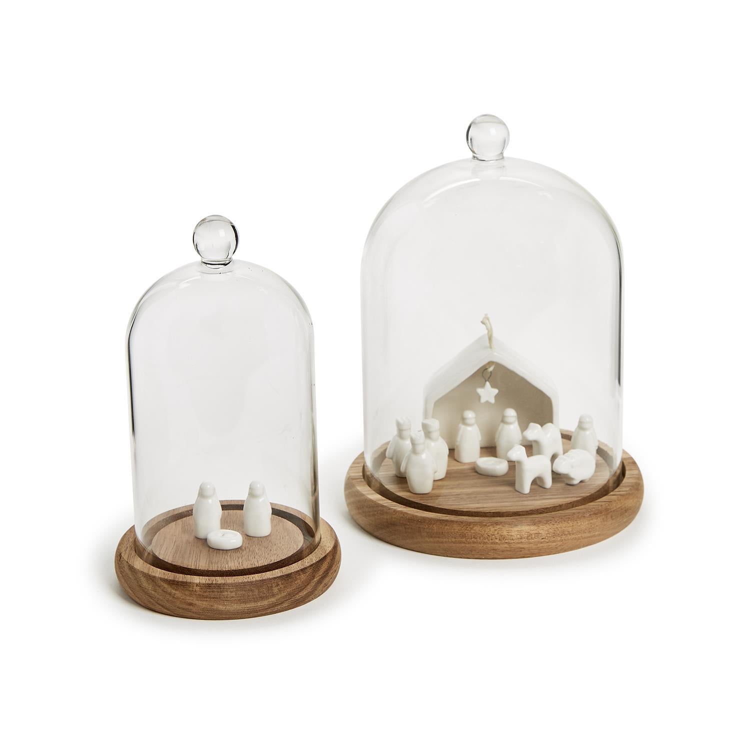 Two glass domes with wooden bases containing small figurines on a white background