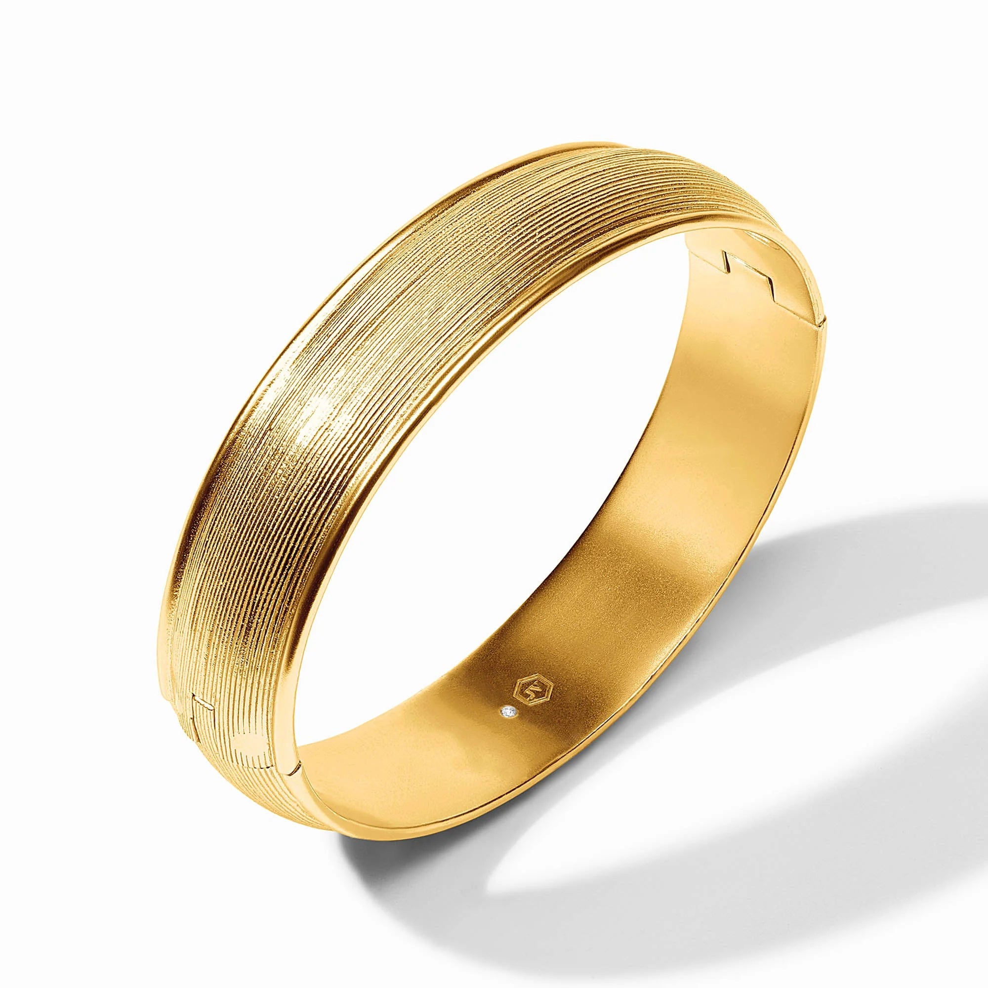 A wide, polished gold bangle bracelet with a textured, horizontally grooved exterior and a smooth, polished interior, shown on a clean white background with a soft shadow.