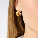 Gold hoop earring worn by a person with long hair on a white background