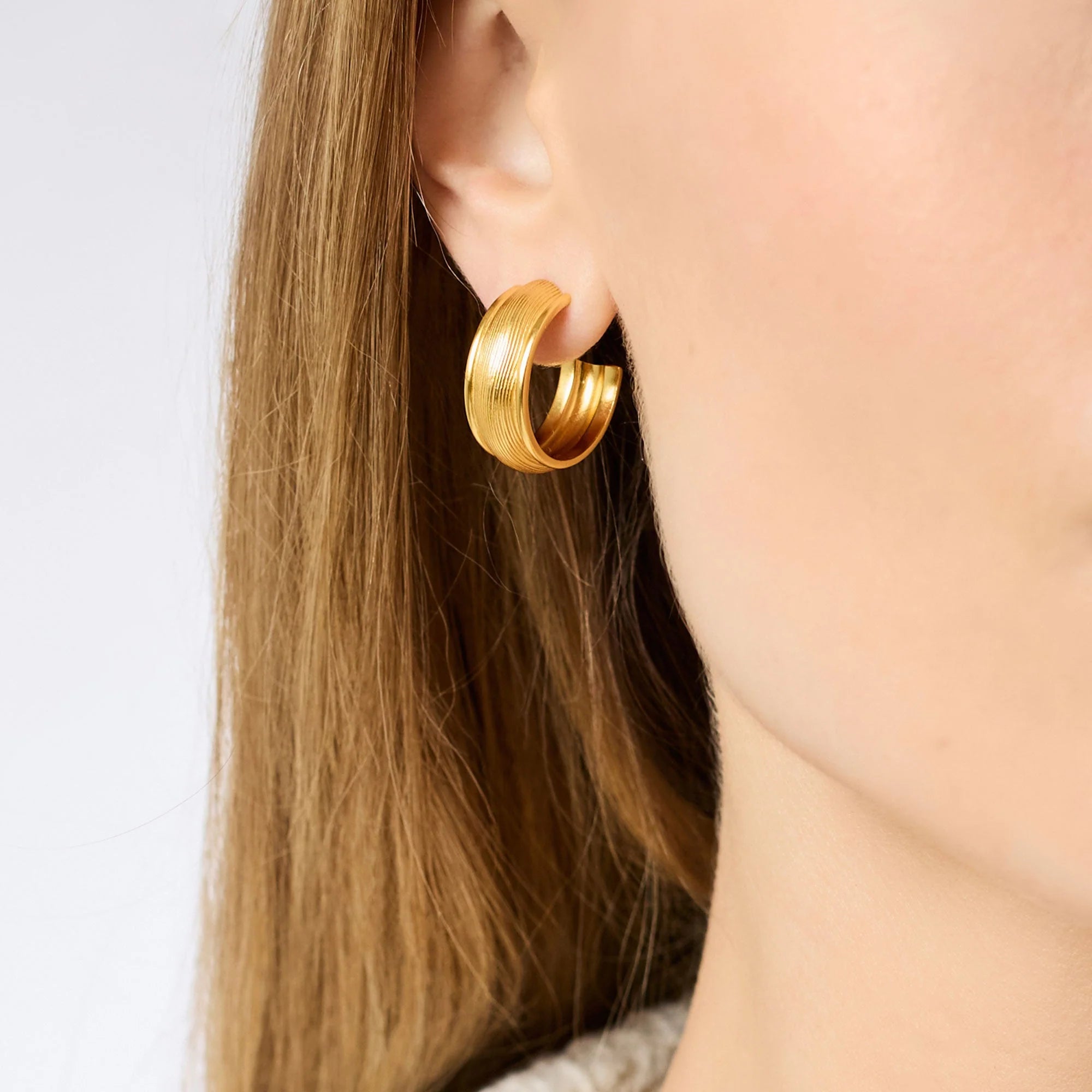 Gold hoop earring worn by a person with long hair on a white background