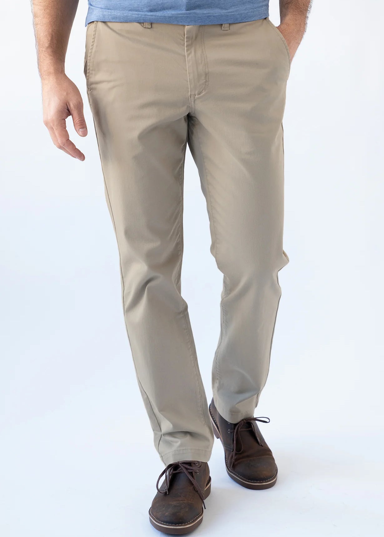 A person wearing beige straight-leg chinos with a blue t-shirt and brown leather shoes, shown from the waist down against a white studio background.
