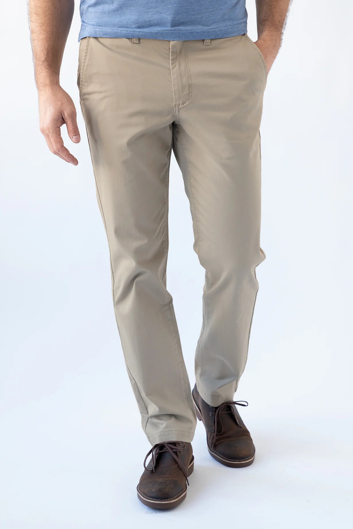 A person wearing beige straight-leg chinos with a blue t-shirt and brown leather shoes, shown from the waist down against a white studio background.