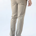 A man viewed from the back wearing beige slim-fit chino pants, a light blue t-shirt, and dark brown leather loafers, set against a plain white studio background.