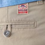 Close-up of khaki chino pants showing a Devil Dog Chino brand patch, a buttoned welt pocket, and a blue striped shirt tucked into the waistband.