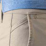 Close-up of the back waistband and pocket area of light beige chinos, showing a blue textured shirt tucked in.