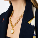 Gold chain necklace with a pendant worn by a person in a dark blazer.