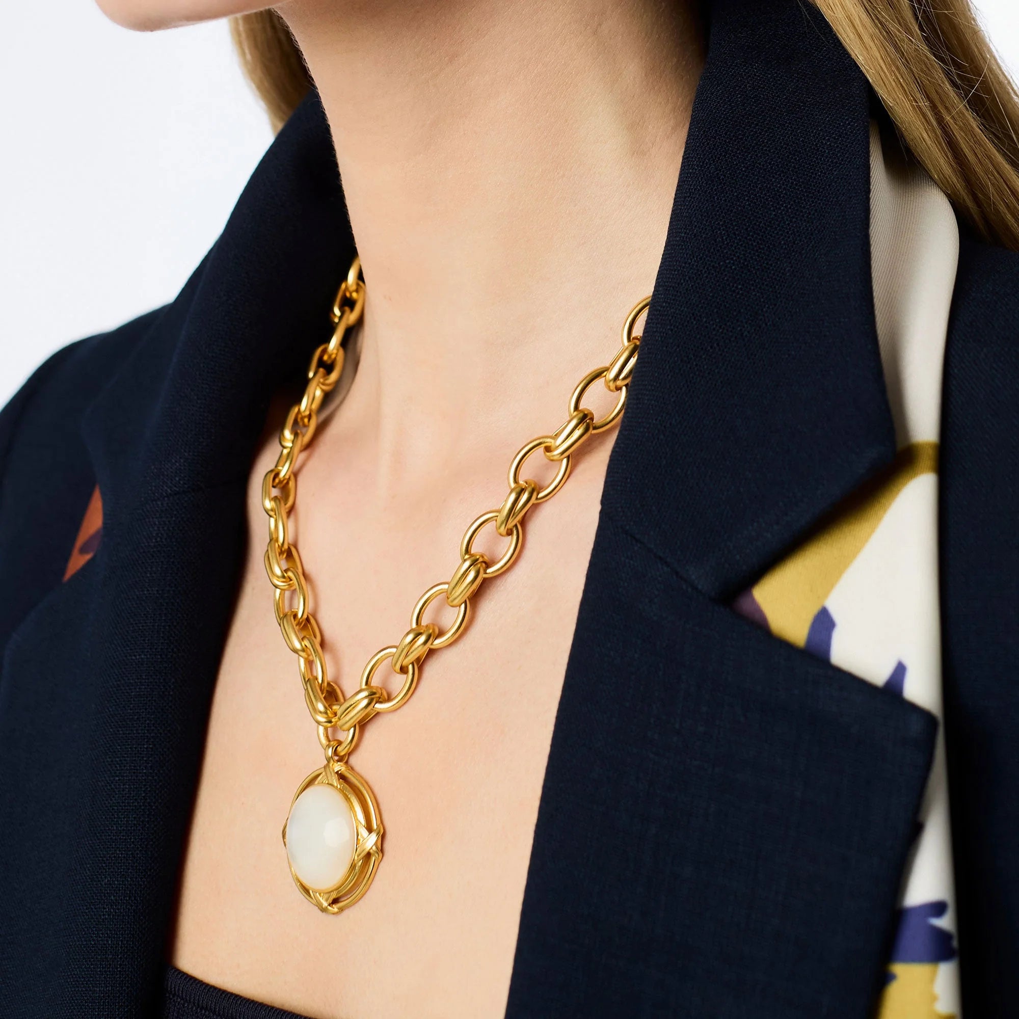 Gold chain necklace with a pendant worn by a person in a dark blazer.