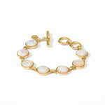 A gold-tone bracelet featuring seven oval iridescent white mother-of-pearl cabochons, a toggle clasp, and a small round logo charm, displayed on a clean white background.