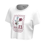A white short-sleeve cropped t-shirt with a vintage-style graphic print on the front. The graphic features a maroon border, stylized flowers in blue and maroon, and the text 'EST.