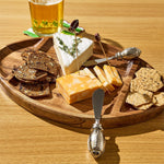 Wooden cheese board with assorted cheeses, crackers, and a glass of beer on a wooden table.