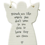 A white ceramic angel-shaped hanging ornament with black printed text that reads, 'Friends are like angels you don't have to see them to know they are there' and a small heart at the bottom, shown on a white background.