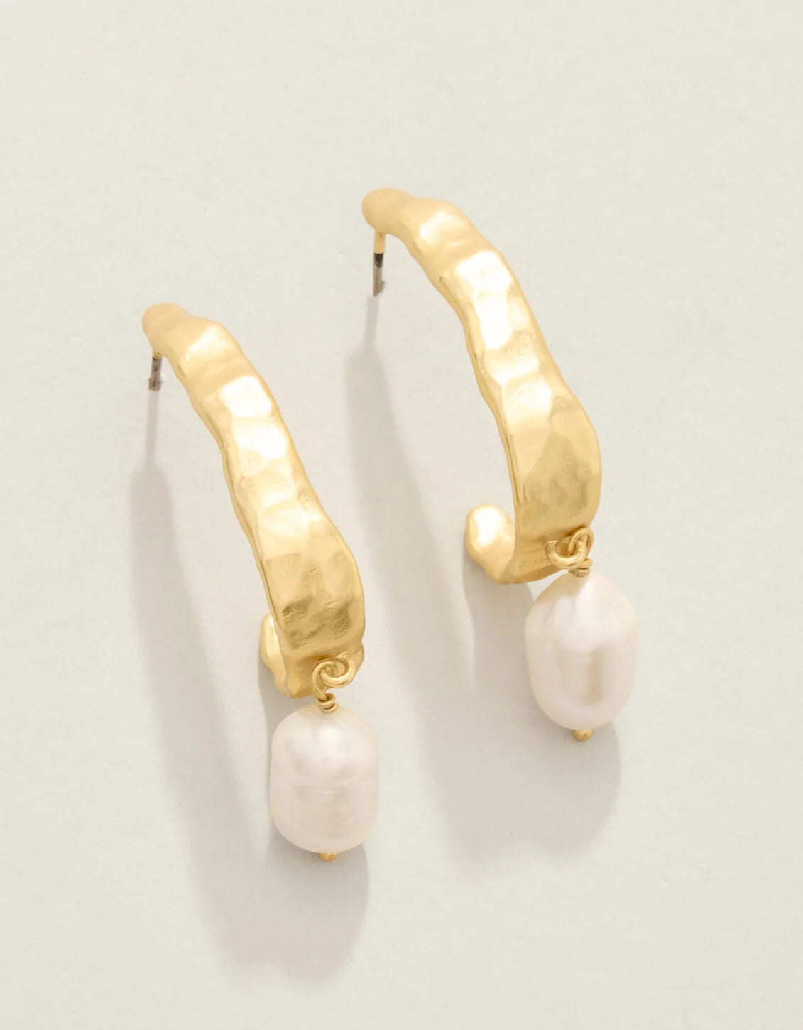 Gold hoop earrings with pearl drops on a light gray background