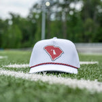A white baseball cap with a red logo on the front, resting on a green athletic field with blurred trees in the background.