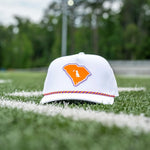 A white trucker-style baseball cap with an orange South Carolina logo patch, resting on a green grass field with white yard lines and a blurred background of trees and stadium lights.