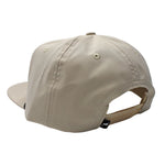 A light beige baseball cap shown from a rear three-quarter angle, featuring a structured six-panel crown, a flat brim, and an adjustable fabric back strap with a small black tag.