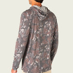 A man wearing a long-sleeve hooded shirt with a brown and gray leaf camouflage pattern, shown from a rear three-quarter view against a light gray background.