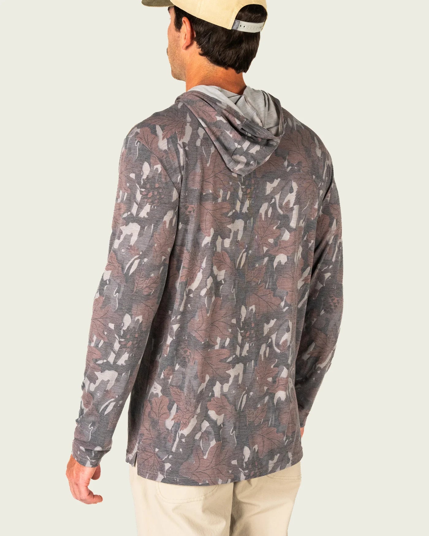 A man wearing a long-sleeve hooded shirt with a brown and gray leaf camouflage pattern, shown from a rear three-quarter view against a light gray background.