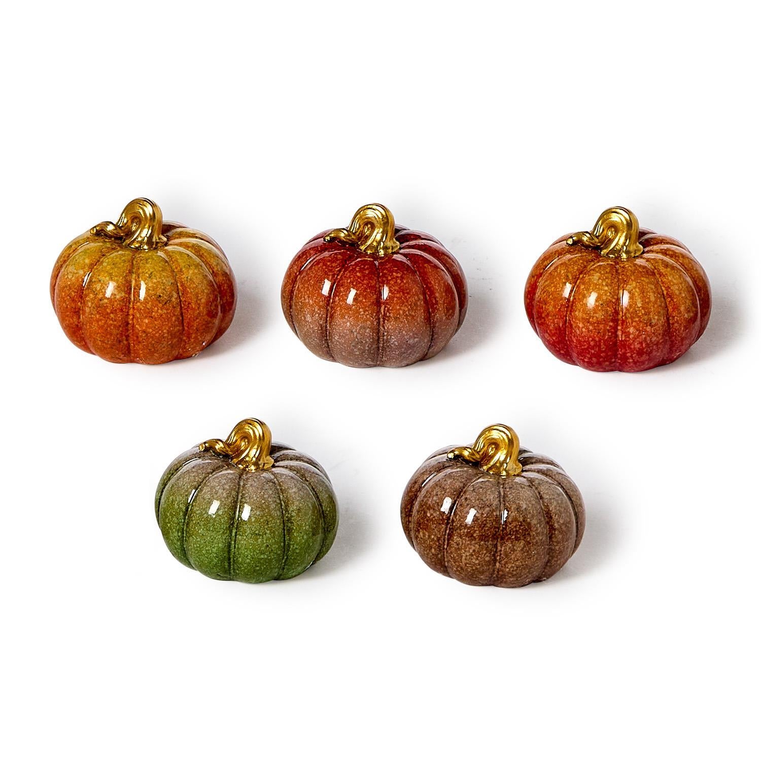 Five glass pumpkins in various colors on a white background