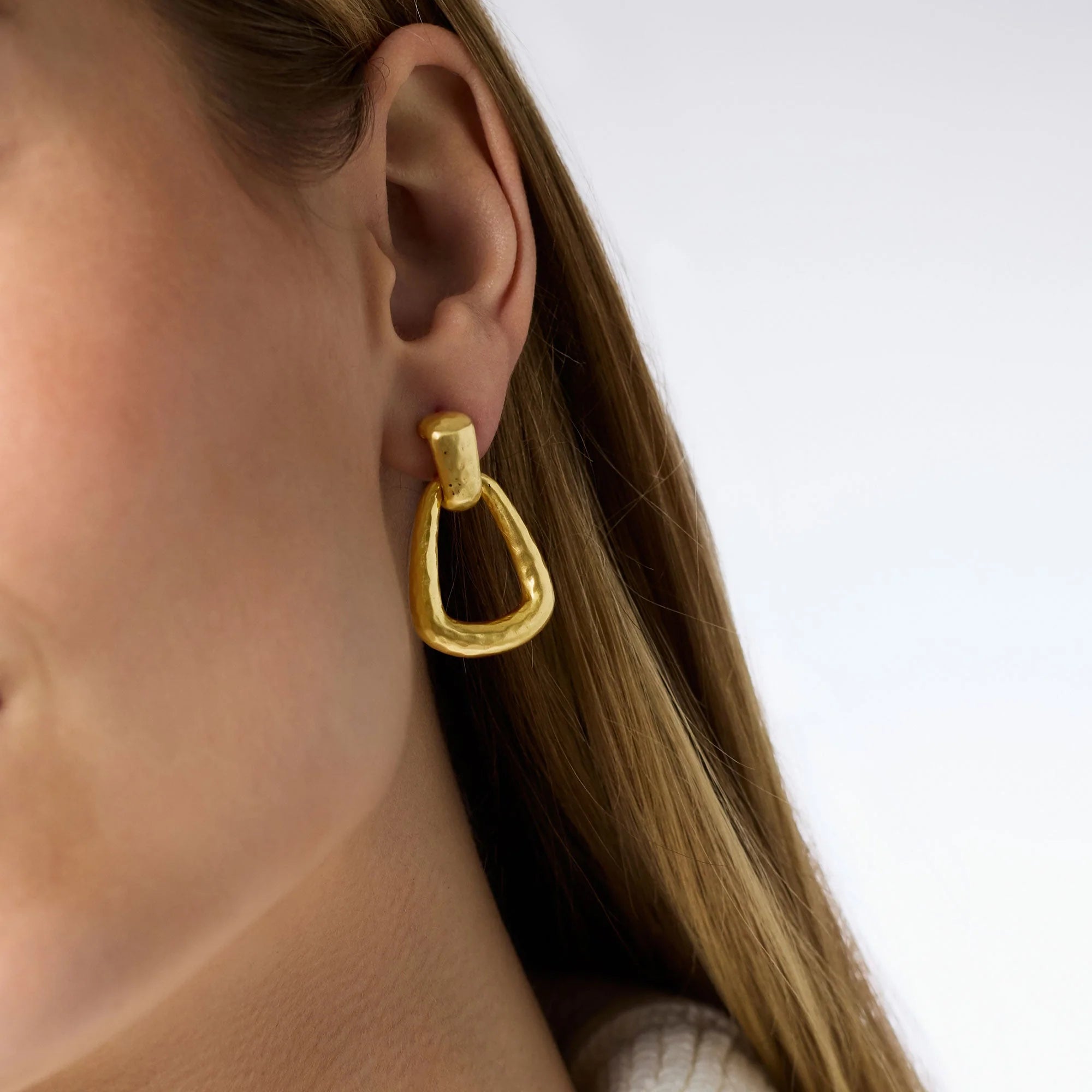 Gold hoop earring worn by a person with a neutral background