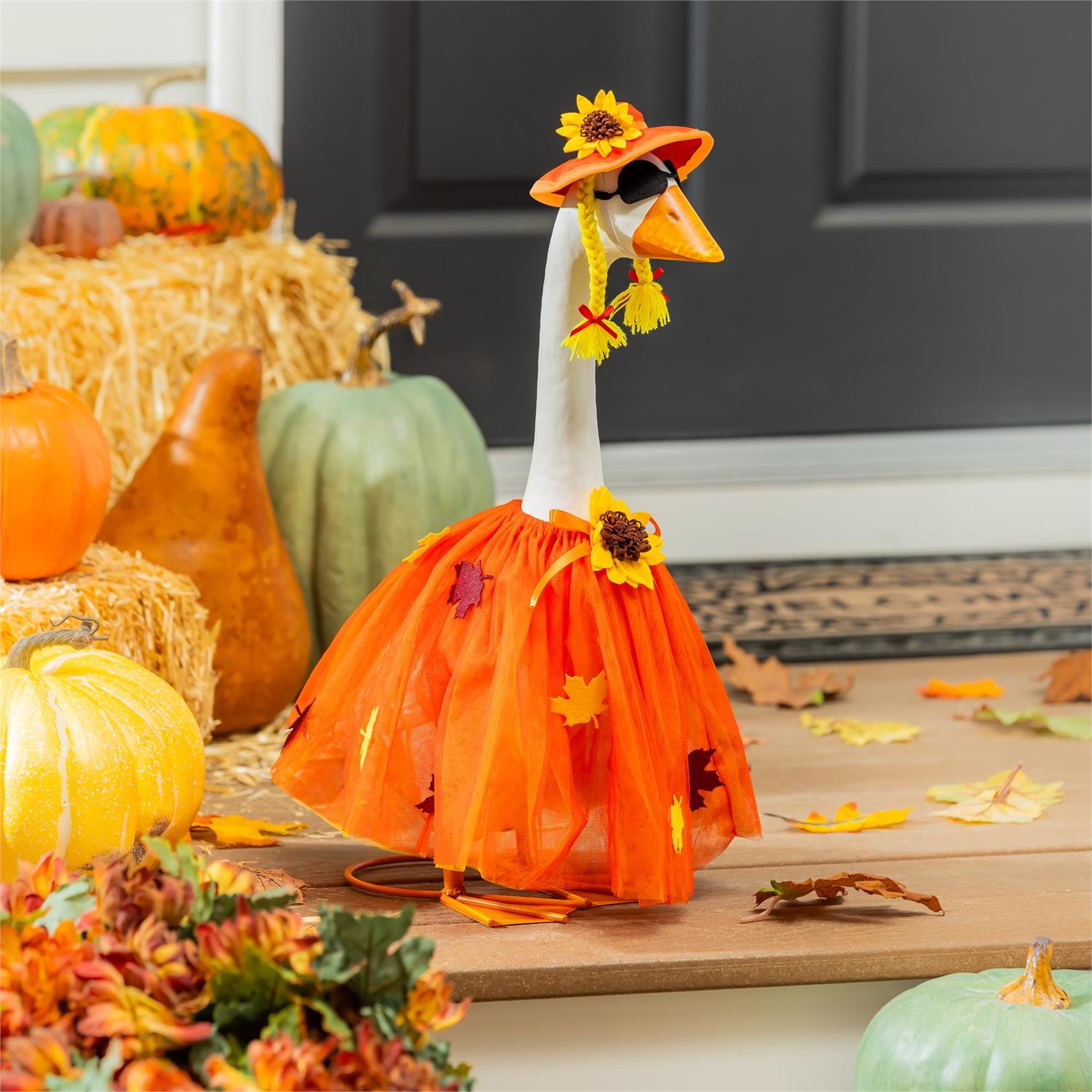 Decorative goose in an orange outfit with sunflower decorations, surrounded by pumpkins and fall leaves.