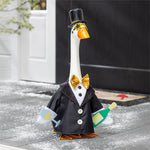 Decorative goose figurine in a suit with a top hat and bow tie, holding a bottle and glass, on a snowy ground.