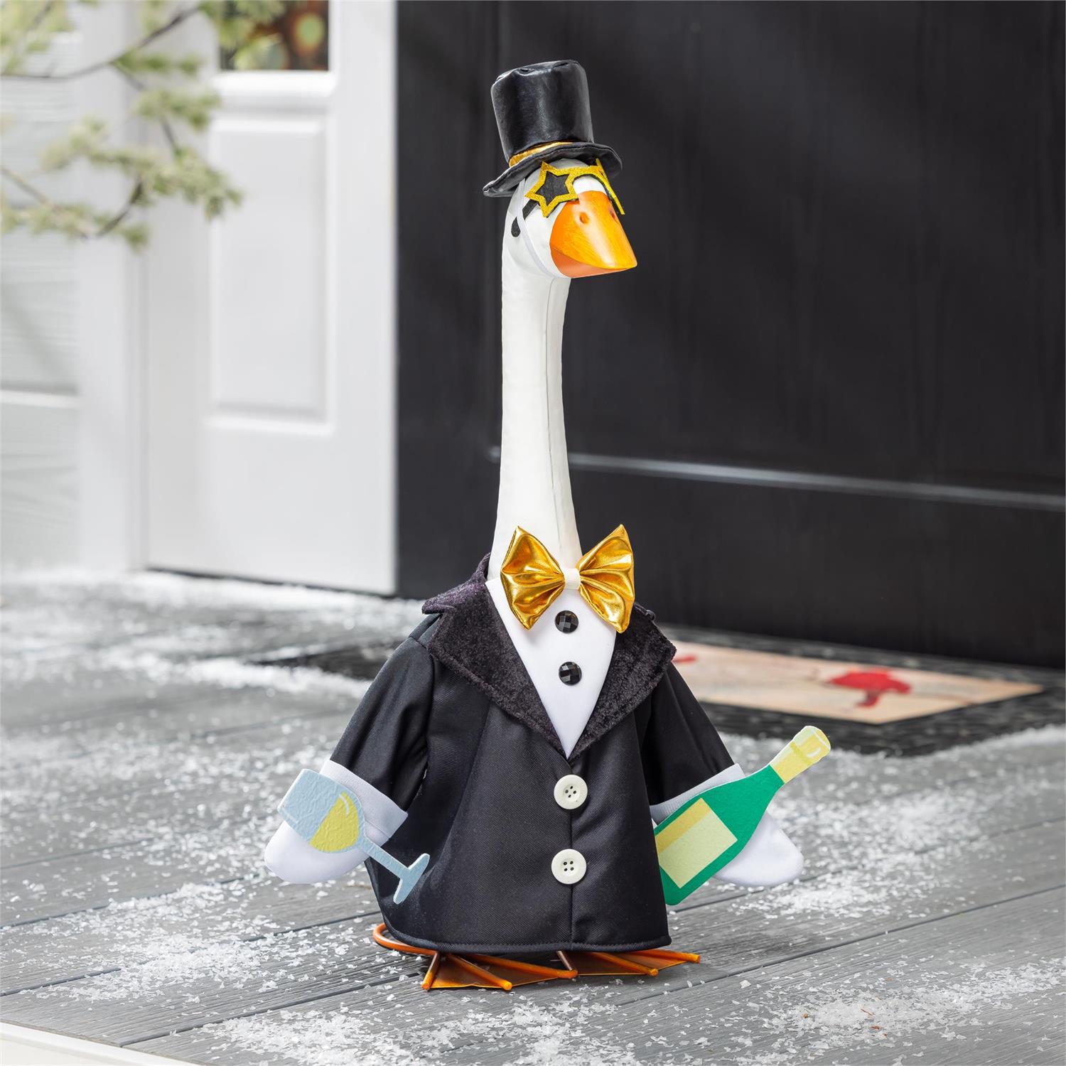 Decorative goose figurine in a suit with a top hat and bow tie, holding a bottle and glass, on a snowy ground.